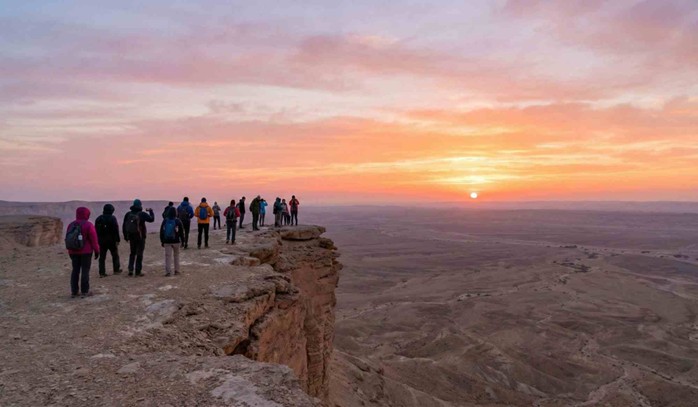 A group of travelers enjoying the stunning sunset view from the cliff edge, a highlight of the Best Edge of the World Riyadh Tours & Packages.