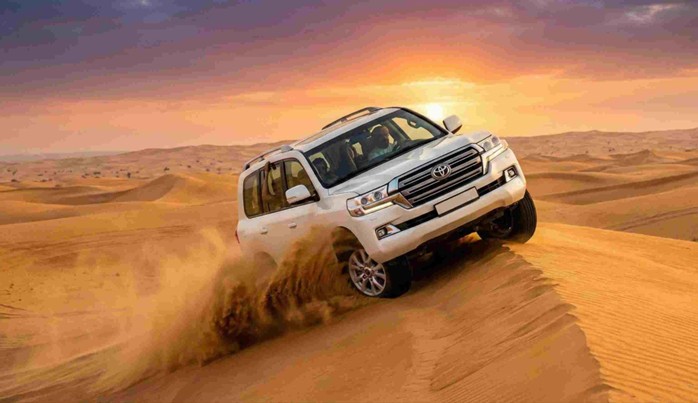 A white 4x4 SUV performing dune bashing, kicking up sand during sunset in the desert, representing popular Evening Desert Safari Riyadh Activities (Dune Bashing, Camel Ride).
