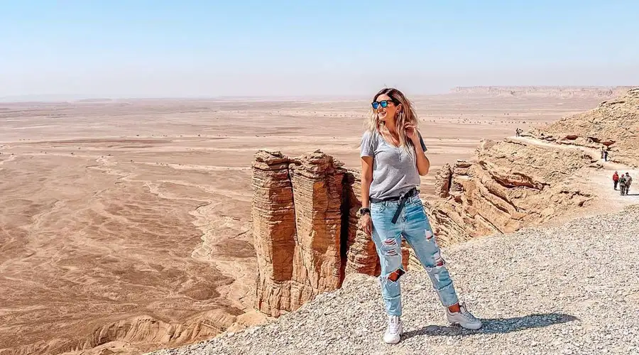 A dark SUV performing a sharp turn on a steep sand dune, kicking up a large cloud of sand.