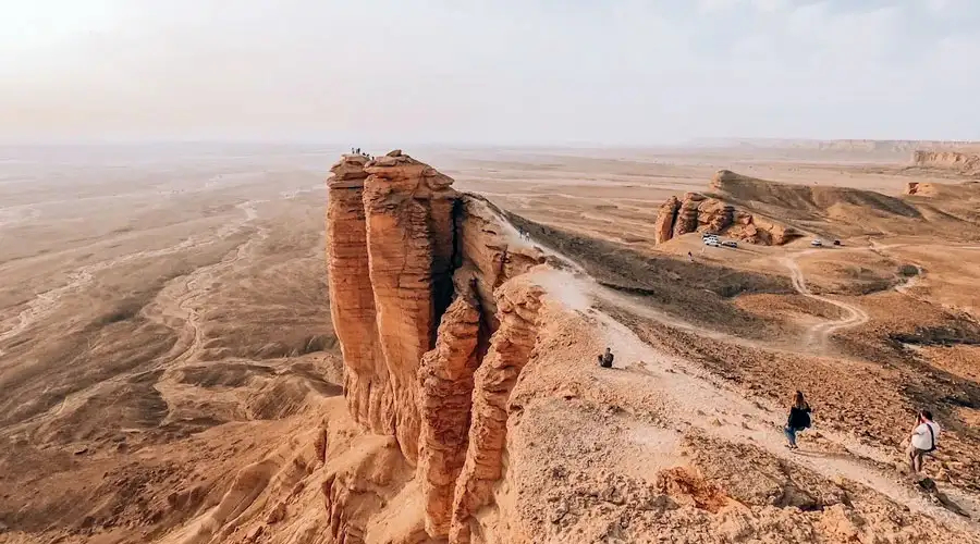 A dark SUV performing a sharp turn on a steep sand dune, kicking up a large cloud of sand.