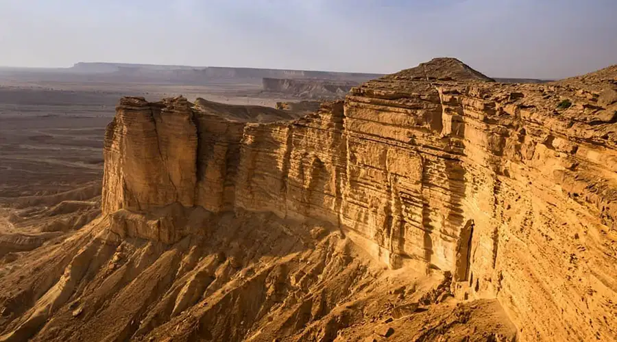 A dark SUV performing a sharp turn on a steep sand dune, kicking up a large cloud of sand.
