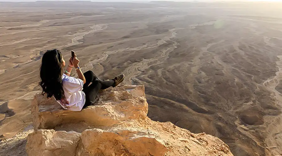 A dark SUV performing a sharp turn on a steep sand dune, kicking up a large cloud of sand.