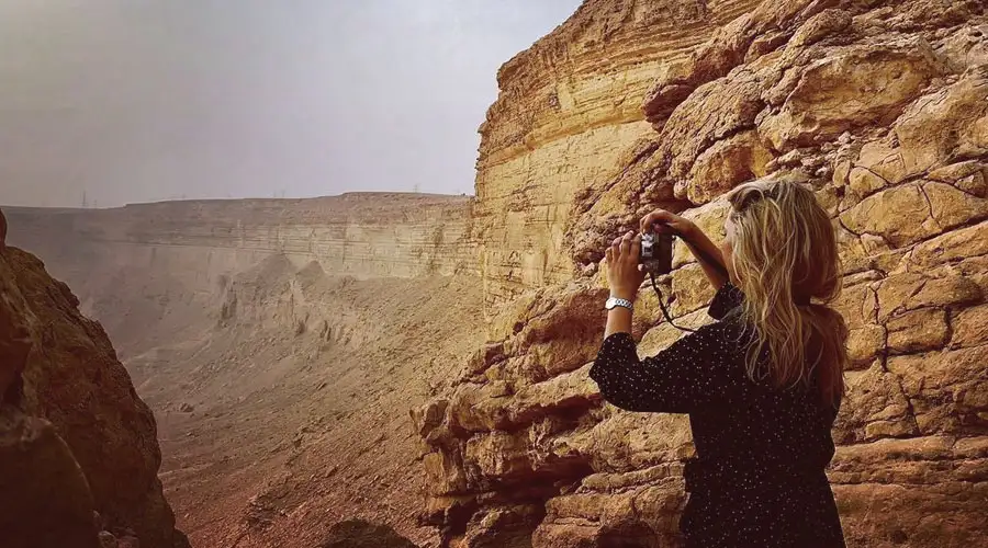 A dark SUV performing a sharp turn on a steep sand dune, kicking up a large cloud of sand.