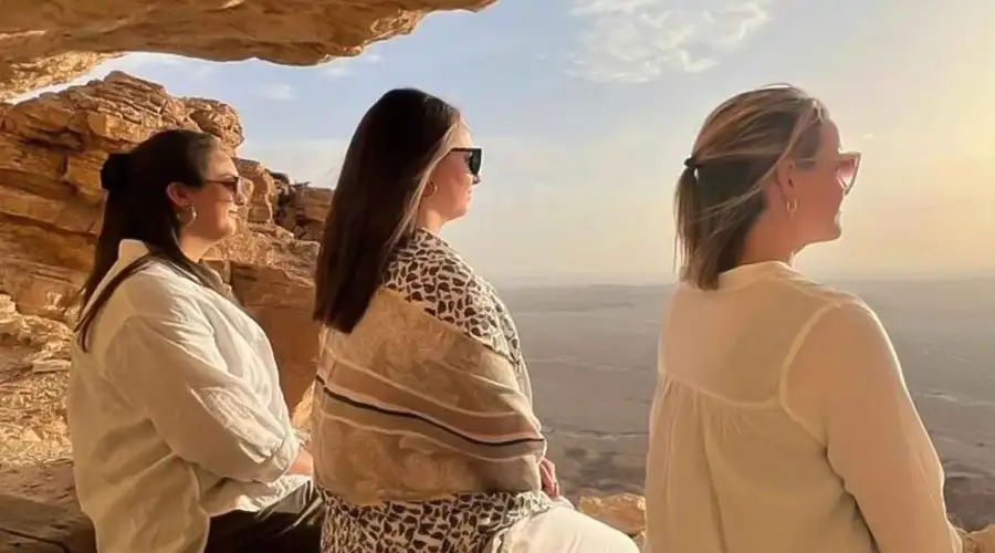 A dark SUV performing a sharp turn on a steep sand dune, kicking up a large cloud of sand.