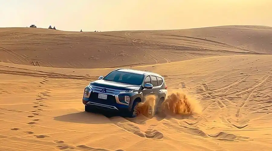 A dark SUV performing a sharp turn on a steep sand dune, kicking up a large cloud of sand.